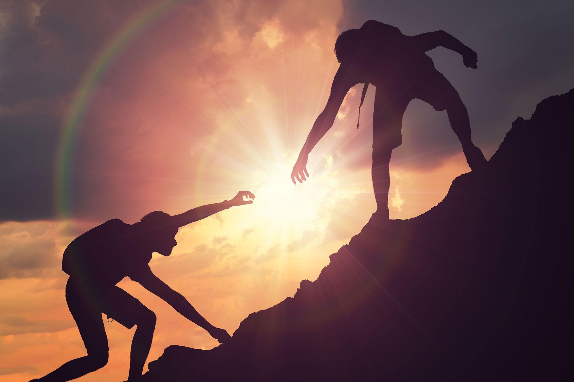 Two hikers helping each other up a mountain