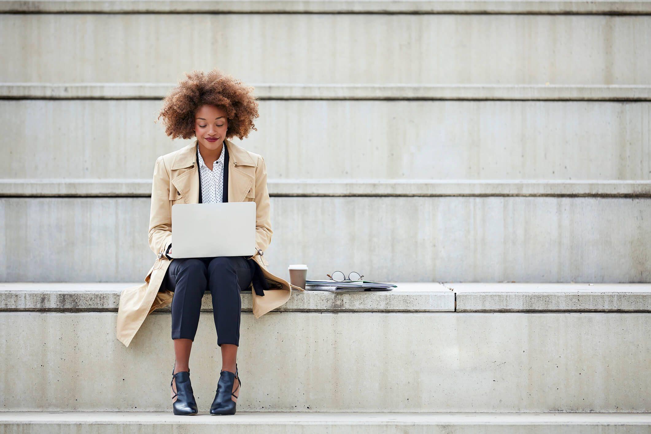 woman sitting on stairs outside working with laptop 