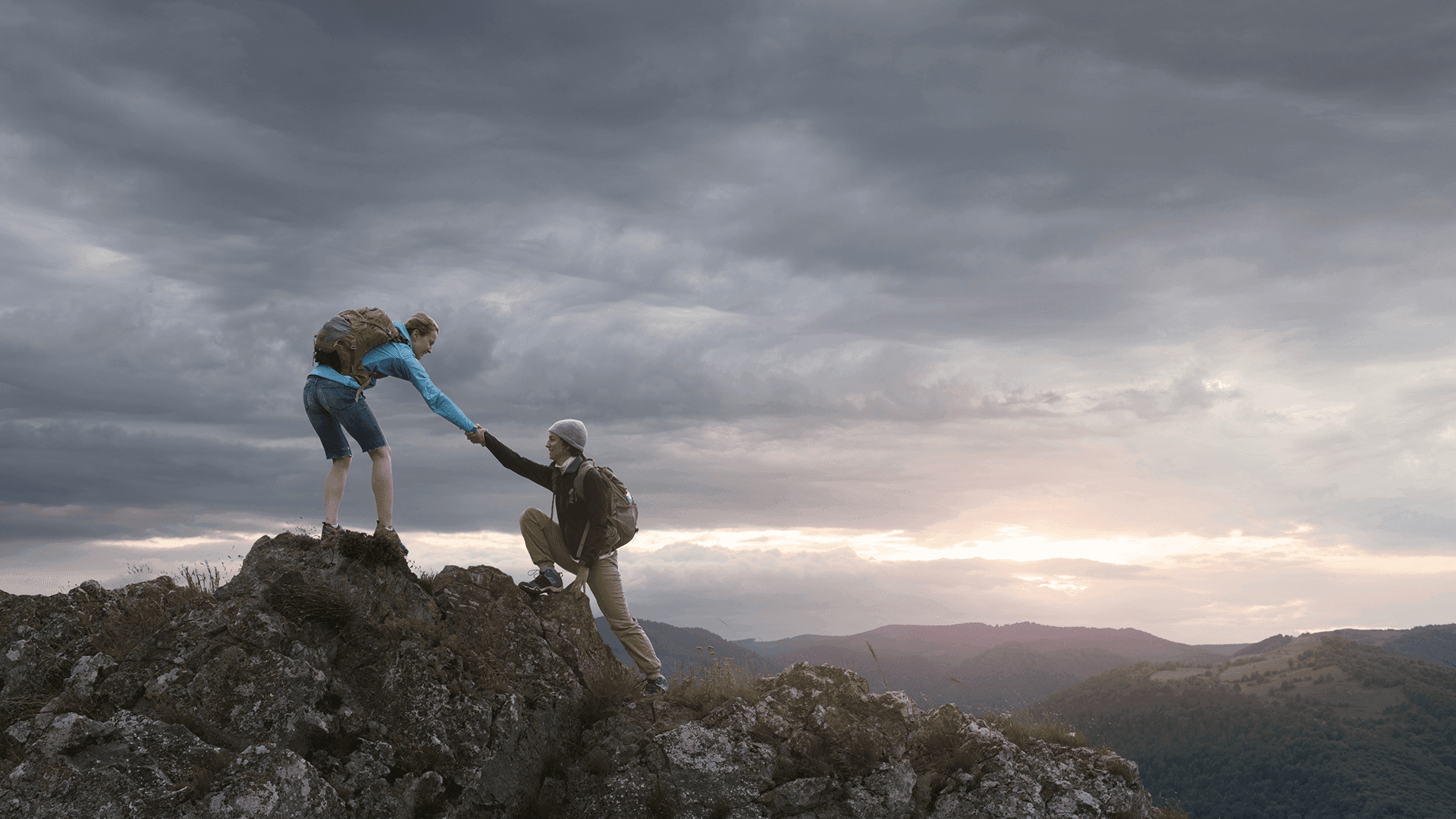 Two hikers helping each other up a mountain