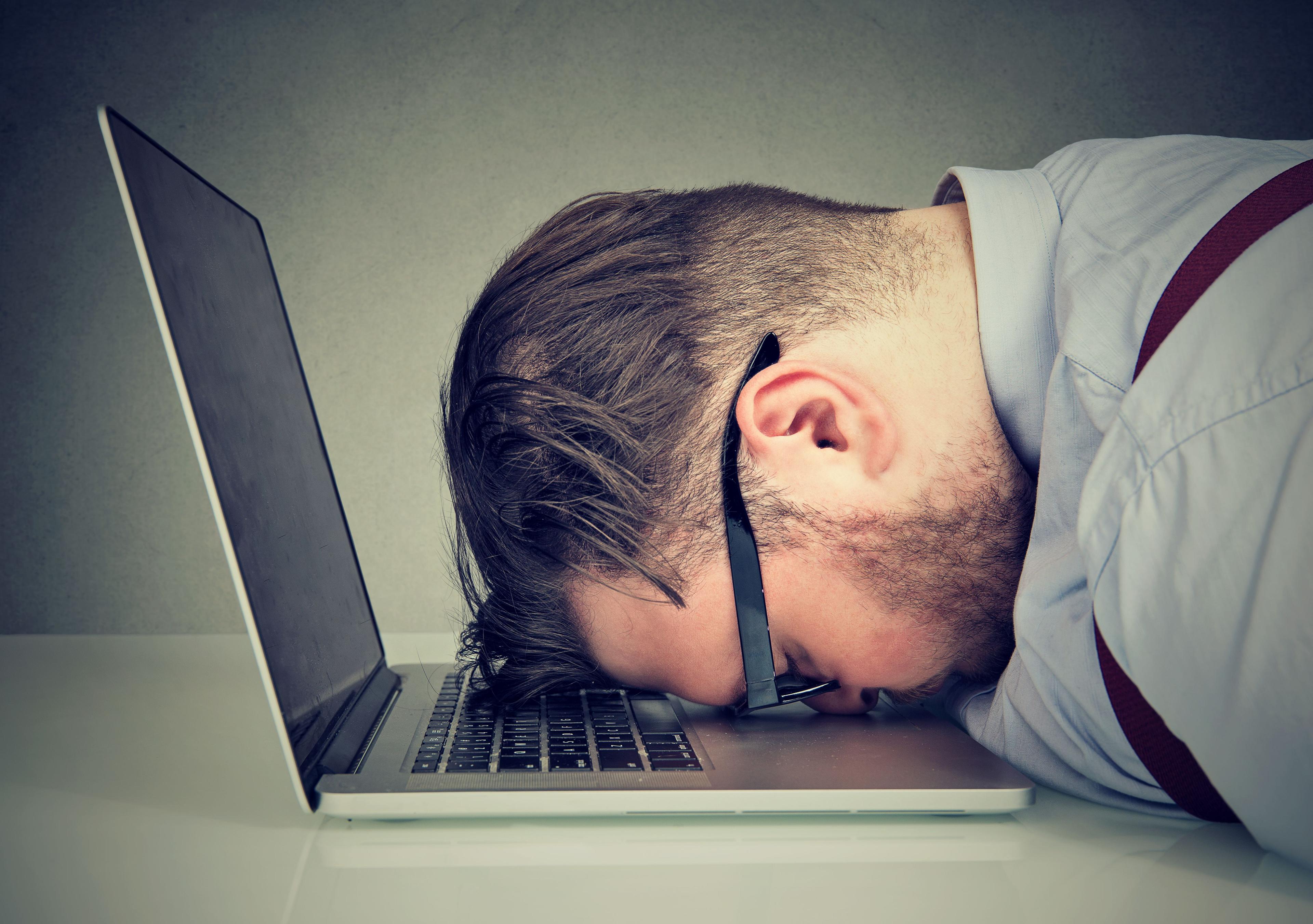 A man puts his head on a laptop keyboard as if giving up